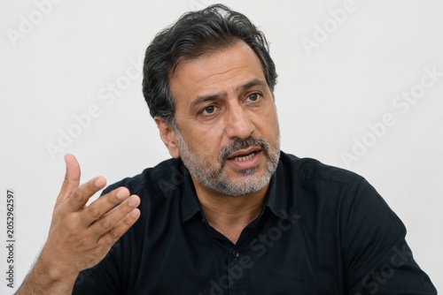 Middle Eastern businessman gesturing in office interview about corporate diversity and equality, middle aged corporate worker