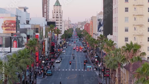 Hollywood Boulevard traffic flowing through Los Angeles with historic buildings, palm trees, illuminated billboards lining bustling urban streetscape