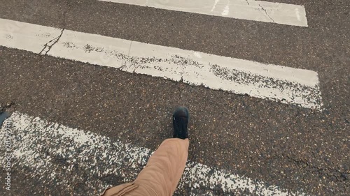A first-person view of feet walking along markings of a worn-out pedestrian crossing. Cracks in asphalt indicate weathering. An urban street scene, focusing on road markings and pedestrian movement