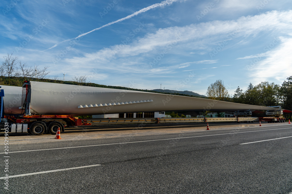 Fototapeta premium Oversized wind turbine blade transported on a specialized trailer along a highway. Renewable energy logistics, heavy haul transport and wind power infrastructure.