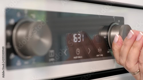 Woman adjusting white oven in kitchen. Female hand pushing and turning knobs on oven control panel. Closeup
