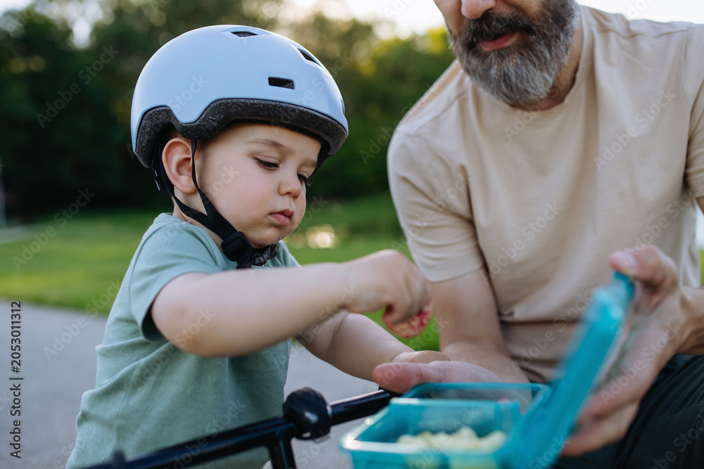 Naklejka premium Little boy having snack while riding bike in park.