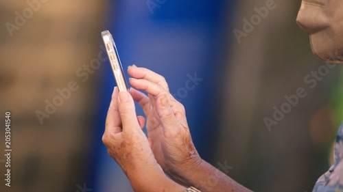 Slow motion senior Taiwanese woman uses a smartphone on a Tamsui street at night, showing older adult adaptation to modern technology, communication, urban life and digital connection