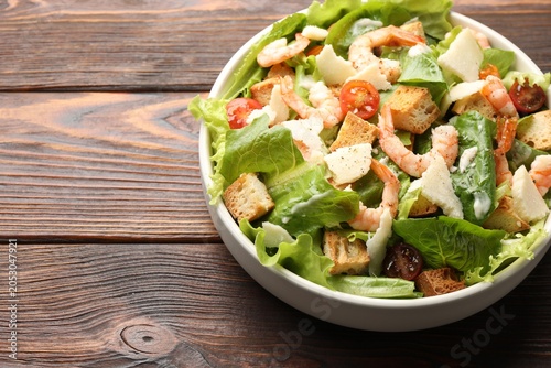 Obraz na płótnie Delicious Caesar salad with shrimps in bowl on wooden table, closeup