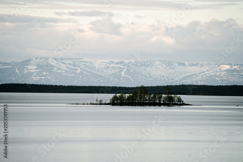 Small forested island on calm lake with distant snowcapped mountains