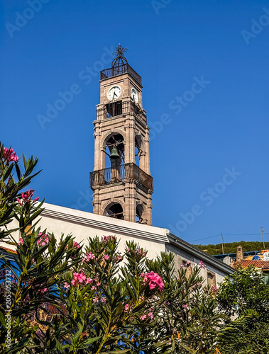 Canakkale, Bozcaada Island, Turkey - July 22, 2024: Clock tower of Greek Orthodox church, known as the Church of the Dormition, death and assumption into heaven, of the Virgin Mary. 