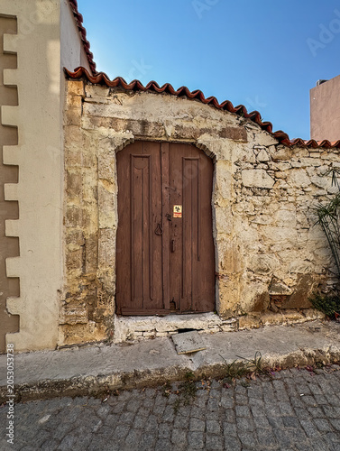 Canakkale, Bozcaada Island, Turkey - July 22, 2024: Dark old double wooden door built in historic yellow stone wall with access to the garden of the house in Ataturk Cd. street