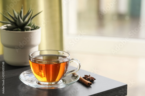 Fotografie Glass cup of hot black tea with cinnamon and star anise on wooden table in room