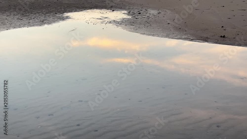 Wolken spiegeln sich in einer Pfütze am Strand im Abendlicht