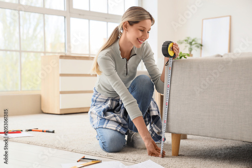 Young woman measuring sofa ...