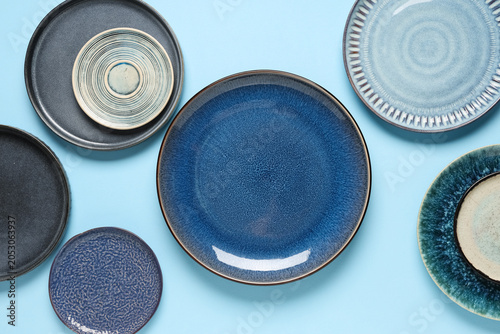 фотографія Assorted ceramic dinnerware collection with blue and gray plates on light blue b