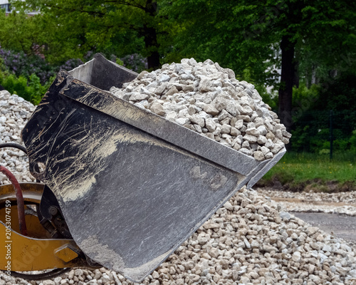 Close up of a wheel loader metal bucket filled with crushed stone at a construction site