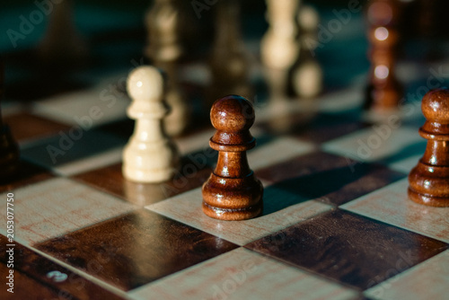Fotografie Dark wooden chess pawn in focus on a chessboard surrounded by blurred pieces