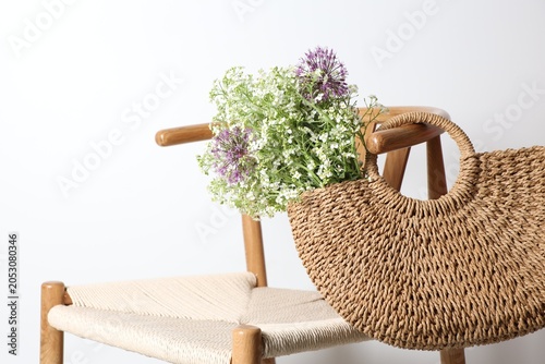 Beautiful wildflowers in bag on chair near light wall, closeup. Space for text
