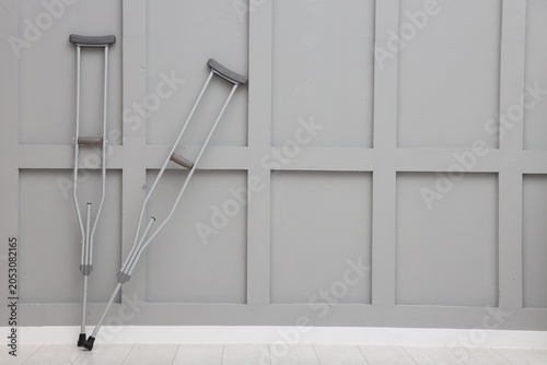 Slika na platnu Metal axillary crutches near grey wall indoors, space for text