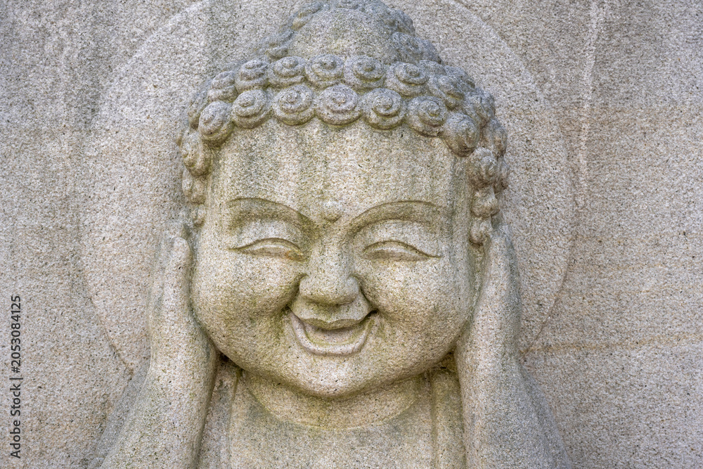 Obraz premium Smiling stone buddha statue covering ears at a korean temple.