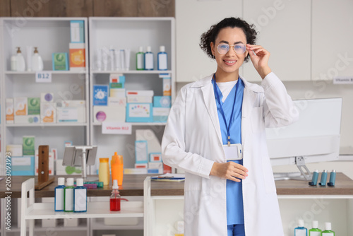 Smiling female pharmacist adjusting glasses in modern pharmacy, healthcare pr...