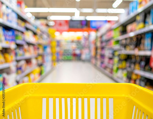 Canvastavla スーパーマーケットの通路と手前の黄色い買い物カゴ　商品が並ぶ棚がボケた店舗内の様子　買い物や節約のイメージ画像　Webサイトやチラシの挿絵に使える販促素材
