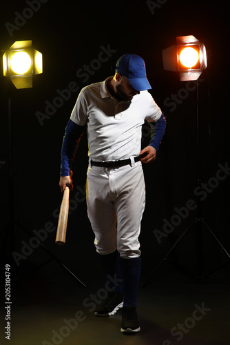 Quadro su tela Baseball player in uniform with bat and cap under studio lights, sports and athl