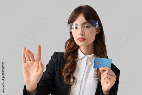 Young businesswoman in AR glasses with credit card using virtual screen on gr...