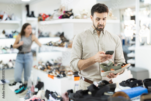 Schilderij op canvas Man buyer scans code on toeless shoes label using smartphone camera and receives detailed information about product on manufacturers website