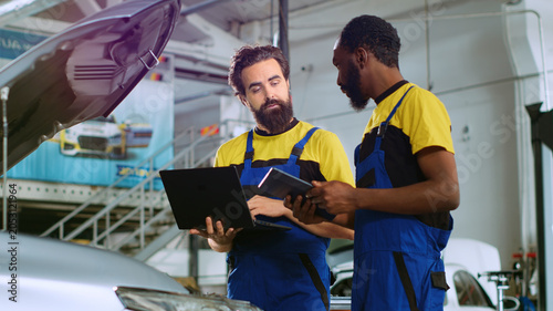 Bild auf Leinwand Mechanics in car service ordering new parts for damaged vehicle using laptop and tablet, with coworkers looking online for components to replace old ones in malfunctioning automobile