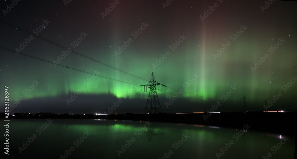 Fototapeta premium Aurora Borealis Behind Power Transmission Tower at Night Reflected in Calm Water
