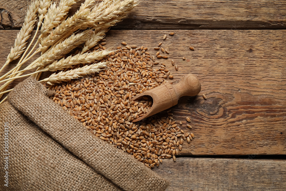 Obraz premium Sack with wheat grains, ears and scoop on wooden background
