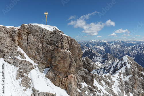 Gipfel der Zugspitze, höchster Berg in Deutschland, mit dem Gipfelkreuz, rechts davon der Jubliäumsgrat, dahinter weitere Gipfel des Wettersteingebirges und der österreichischen Alpen.
