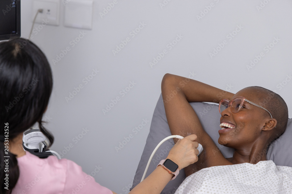Obraz premium Diverse female patient and pink-scrub clinician using probe while reclining on exam bed, copy space