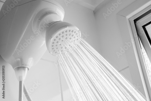 Close-up of a white electric shower head with strong water jets flowing in a modern bathroom interior. 