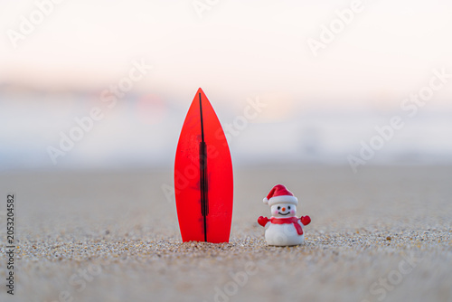 Sandy Christmas Snowman is watching the waves, standing on beautiful beach with a surf board - horizontal version in Patong Beach, Phuket, Thailand