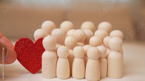 Quadro su tela A hand adds a red heart to a group of wooden figures, symbolizing warmth, love in the community, kindness, emotional connection, mutual support, positive relationships, and social unity