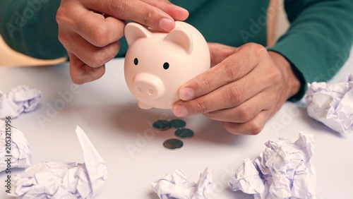 Obraz na płótnie A person puts coins into a piggy bank, but they fall straight through the bottom, symbolizing failed savings, poor financial management, insecurity, and the constant challenge of making ends meet