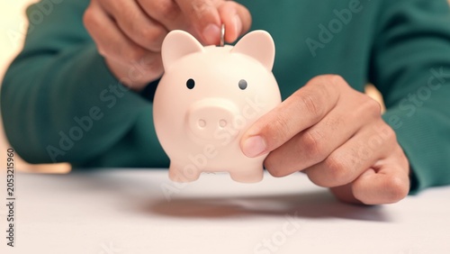 Fotografie A person puts a coin into a piggy bank, but the coin falls straight through the bottom, symbolizing inability to save money, financial leakage, insecurity, and the frustration of unachieved goals