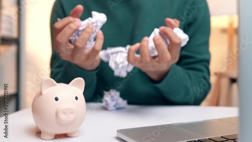 Foto A person crumpling debt bills beside a piggy bank, expressing sorrow and despair, symbolizing financial burden, money stress, emotional struggle, poor debt management, and the need for change