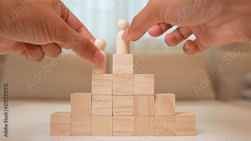 Photography A wooden figure stands atop block steps while another is placed lower, symbolizing career competition, ambition, achievement, personal growth, striving for success, and overcoming challenges