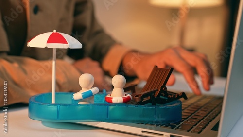 Vászonkép A freelancer places toy swim rings on wooden figures in a mini pool while working, symbolizing the urge for vacation