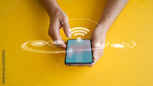 Person holding smartphone with wi-fi signal and on yellow background, mobile phone hands wireless internet