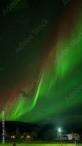 Vertical Time Lapse of Stunning Green and Red Aurora Borealis dancing over some houses in Hofn, Iceland, northern lights video on a starry night