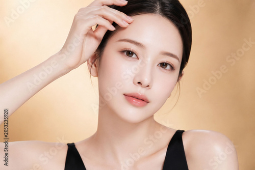 澄んだ視線と均一でなめらかな素肌を印象的に見せる若い女性の洗練されたビューティーポートレート。上品なツヤ感、自然な血色感のあるリップ、すっきりまとめたヘアスタイルとブラックトップスのコントラストが映え、スキンケア、保湿化粧品、美容液、フェイスケア、ラグジュアリーコスメ広告に適した高品質な人物素材