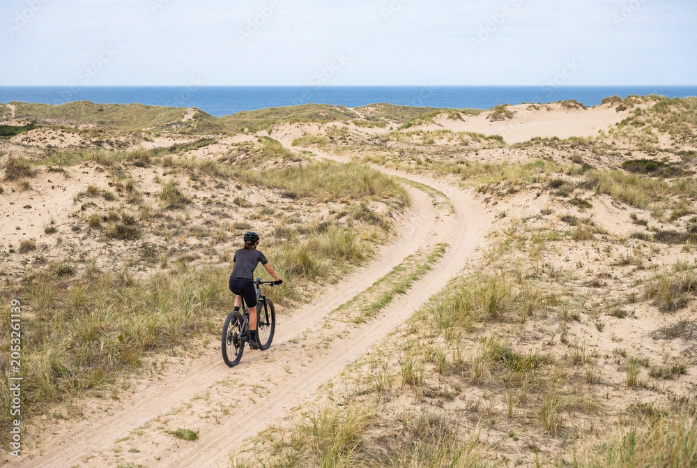 Fototapeta premium Female eMTB Rider Following Coastal Dune‑Side Path