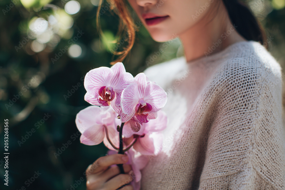 Naklejka premium Female model holding blooming Phalaenopsis amabilis orchid outside in daylight, lifestyle photography