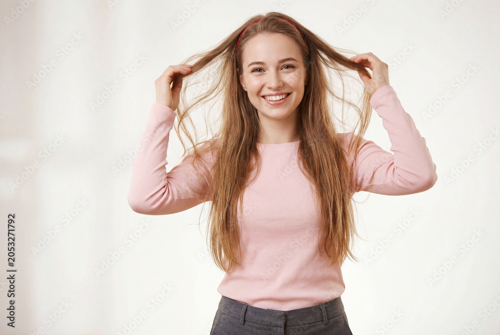 Naklejka premium Joyful young woman wearing a pink top playing with her long brown hair while smiling warmly