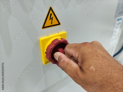 Close-up of worker bare hand turning main isolator switch on electrical panel