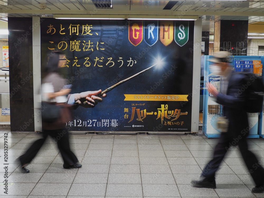 Naklejka premium TOKYO, JAPAN - June 5, 2026: People pass a billboard in a subway station advertising the play Harry Potter and the Cursed Child. It notes that the production is going to close.