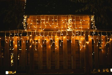 Warm yellow Christmas fairy lights icicles hanging from a wooden fence or cottage roof structure at night.