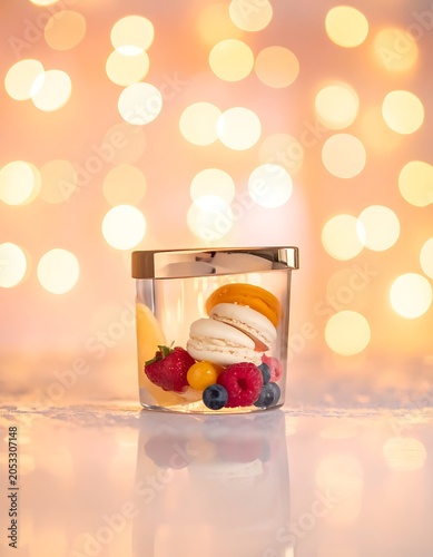 A small glass jar filled with macarons and fruits on a shiny surface