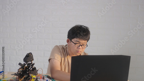 Asian young student using a laptop at home while working on a robotics project with electronic components and robotic devices. Concept of STEM education, coding, and technology learning.