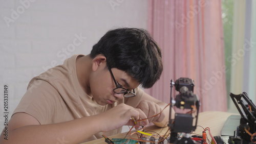 Asian young student wiring a robotics project at home with robotic devices, electronics, and a laptop. Concept of STEM education, engineering skills, innovation, and hands-on technology learning.